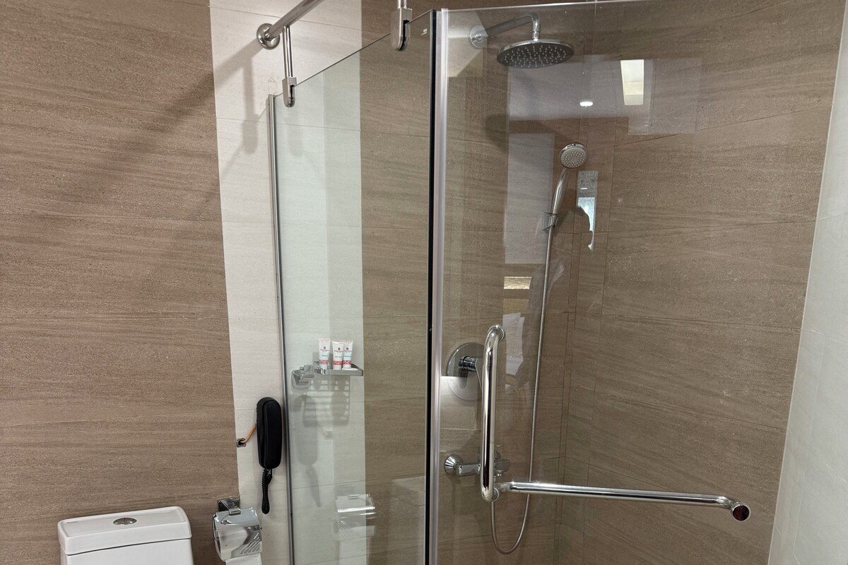 A modern bathroom with a glass-enclosed shower, a toilet, and a hand dryer.