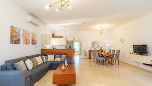 Una sala de estar moderna con un sofá seccional gris, una mesa de centro de madera, y un comedor con mesa y sillas de madera.