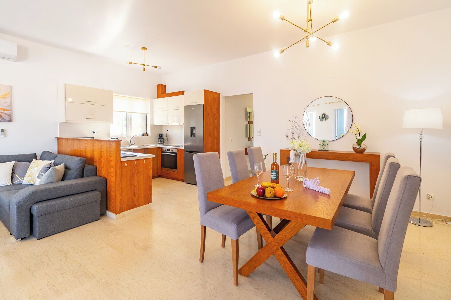 A modern living room with a grey sofa, wooden dining table, and a kitchen in the background.