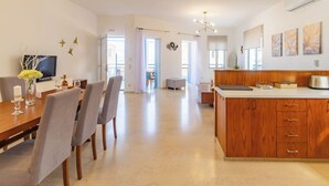 Una cocina moderna con armarios de madera, un comedor con mesa y sillas, y una sala de estar con televisor y objetos decorativos.