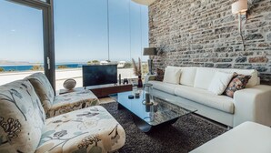 A modern living room with a stone wall, a sofa, a coffee table, and a view of the sea. - Villa Kera Panorama - villa with pool, Crete (Vámos)