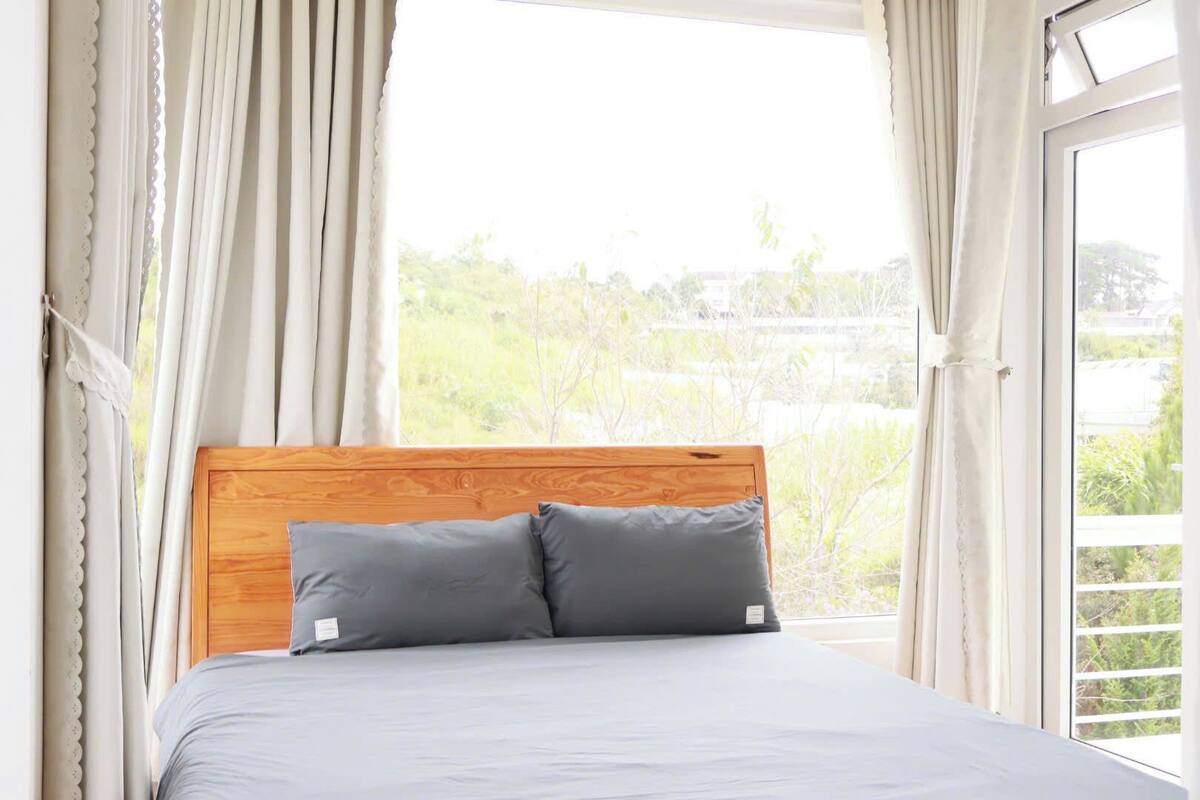 A bed with a wooden headboard and two pillows, set against a window with curtains.