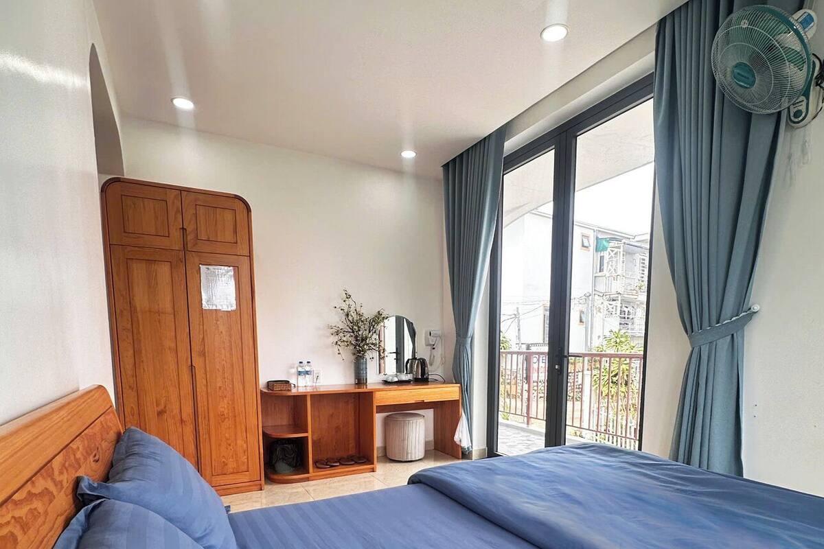 A bedroom with a bed, wooden wardrobe, desk, and a balcony with a view.