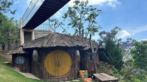 Une maison de style hobbit, avec une porte ronde, un banc en bois et un chemin de pierres menant à l’entrée.