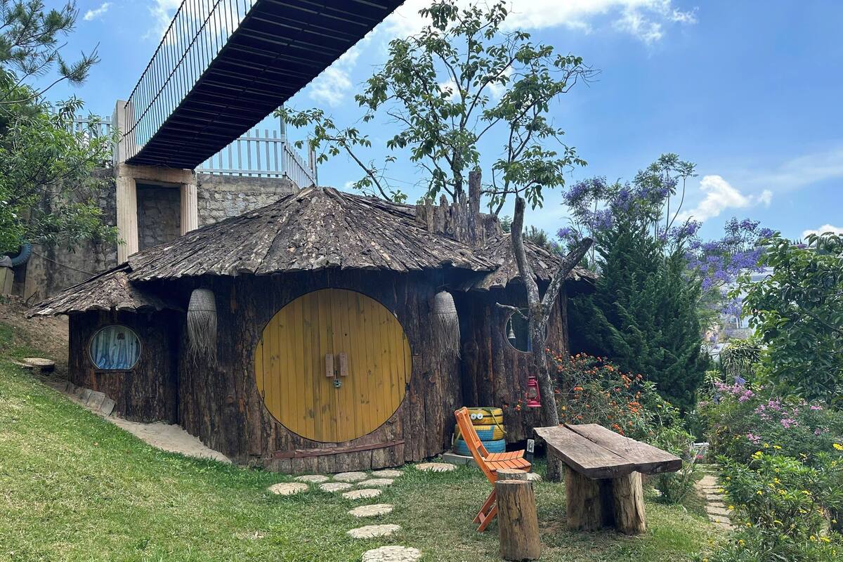 A Hobbit-style house with a round door, a wooden bench, and a stone path leading to it.