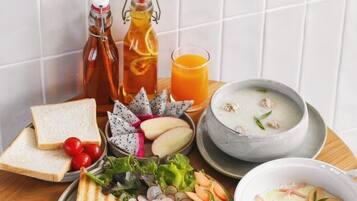 A breakfast spread on a wooden table including toast, eggs, sausages, and a bowl of soup.
