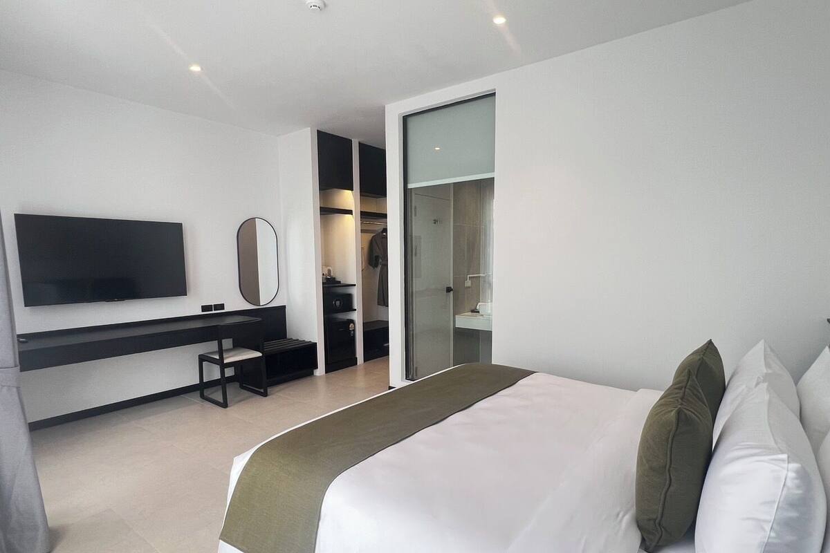 Ein modernes Hotelzimmer mit einem großen Bett, einem an der Wand befestigten Fernseher, einem Schreibtisch mit Stuhl und einem begehbaren Kleiderschrank.