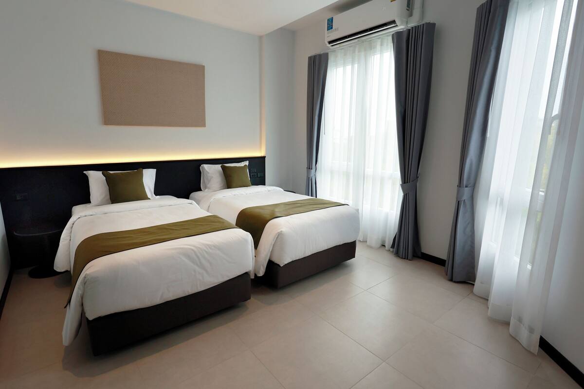 Ein Hotelzimmer mit zwei Betten, einem großen Fenster mit Vorhängen, einer Klimaanlage und einem Wandbild.