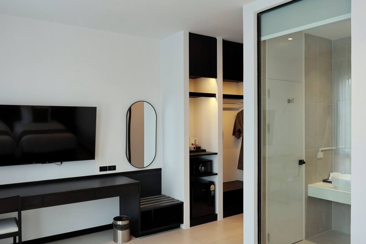Ein modernes Hotelzimmer mit Flachbildfernseher, großem Spiegel, Kleiderschrank und Duschkabine aus Glas.