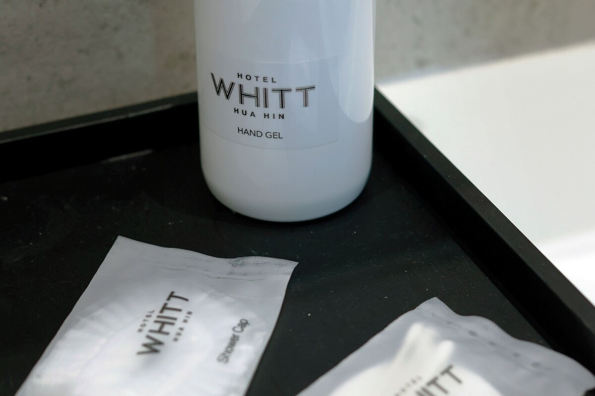 Une bouteille blanche de gel hydroalcoolique de la marque Hotel Whittt et deux sachets du même produit, le tout posé sur un plateau noir.