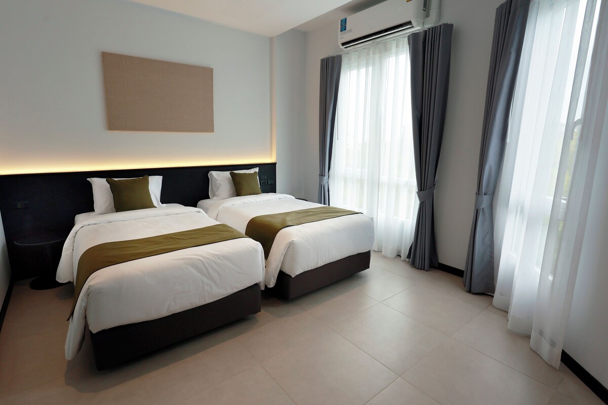 Une chambre d’hôtel avec deux lits, une grande fenêtre avec des rideaux, un appareil de climatisation et une œuvre d’art accrochée au mur.