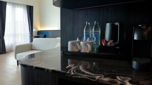 Ein modernes Hotelzimmer mit Marmorplatte, einer Sitzecke mit Sofa und einer Kaffeestation mit Getränken und Snacks.
