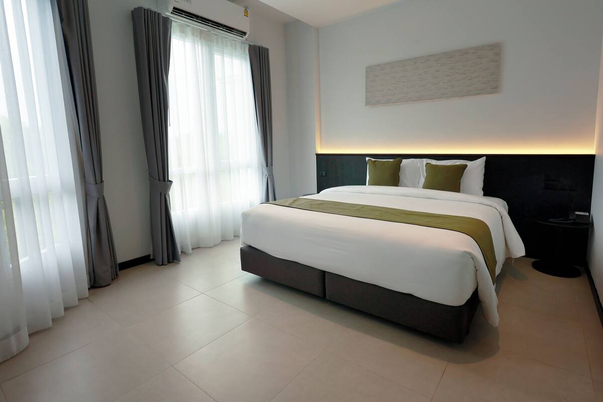 Ein modernes Hotelzimmer mit einem großen Bett, einem Nachttisch, einem Wandbild und einem Fenster mit Vorhängen.