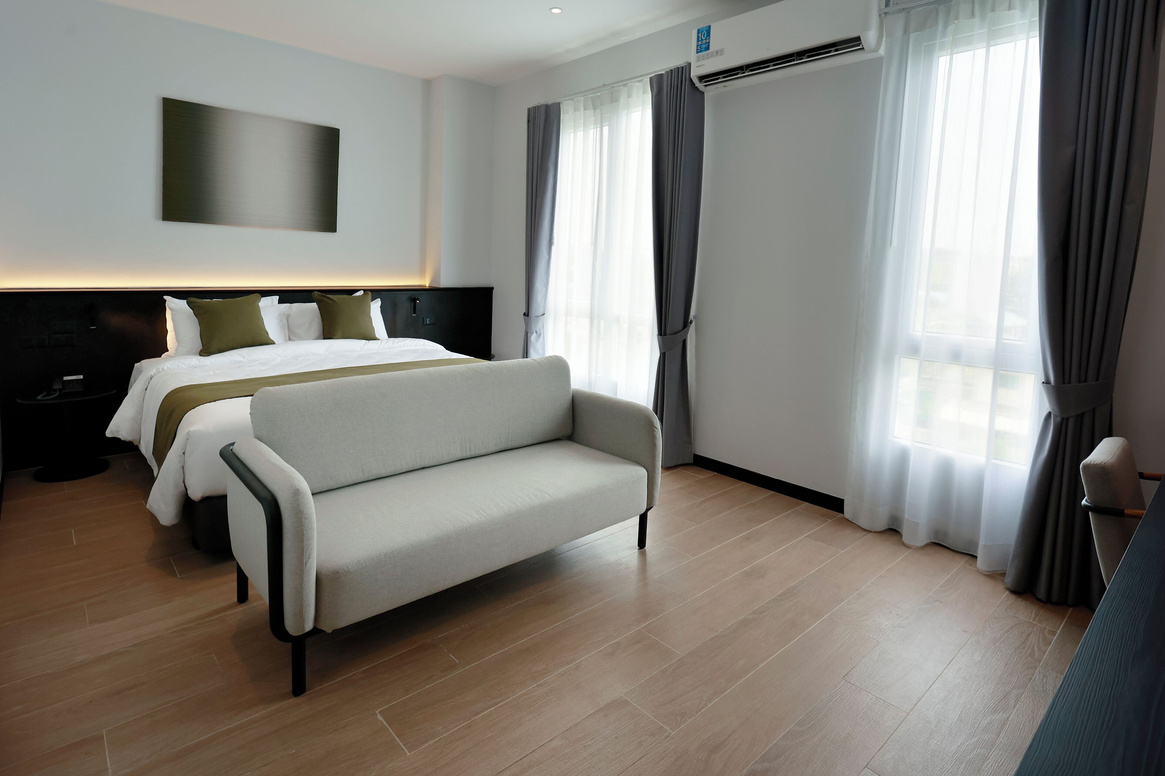 A modern hotel room with a large bed, a sofa, a TV, and a window with curtains.