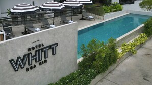 Ein Hotel mit Schwimmbad, Außenbereich mit Sonnenschirmen und einem Schild mit der Aufschrift 'Hotel WHITT'.