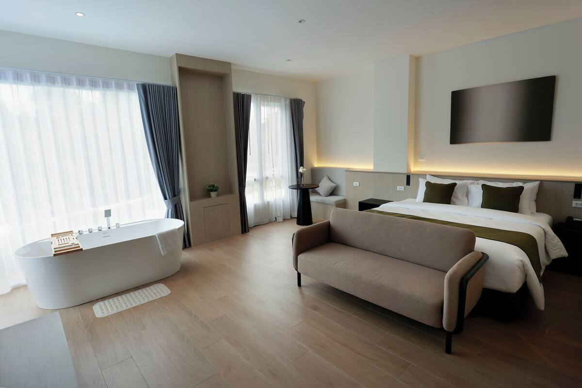 Ein modernes Hotelzimmer mit einer großen Badewanne, einem Sofa, einem Bett mit vielen Kissen und einem an der Wand befestigten Flachbildfernseher.