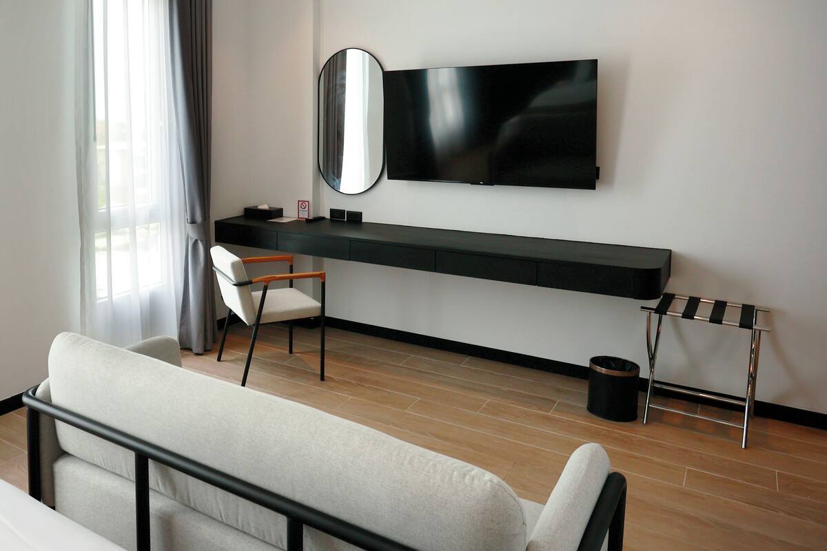Ein modernes Hotelzimmer mit Flachbildfernseher an der Wand, Holzboden, einer Couch, einem Sessel und einem kleinen Tisch mit Spiegel.