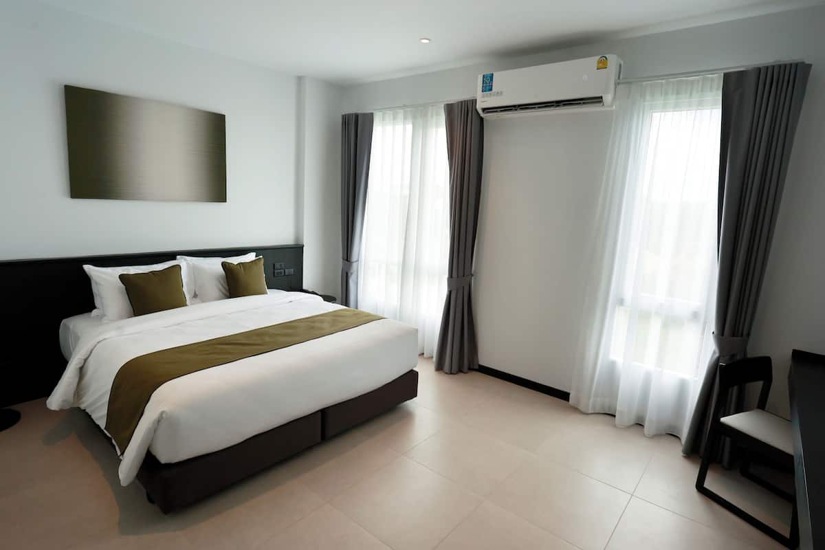A modern hotel room with a large bed, air conditioning, curtains, and a desk.