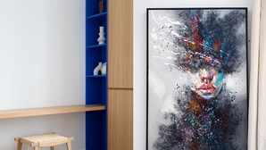 Ein Zimmer mit einer hölzernen Bank, einem blauen Regal und einem großen abstrakten Gemälde an der Wand.