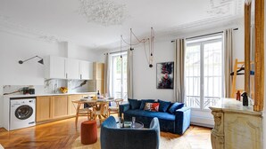 Ein modernes Wohnzimmer mit einer Couch, einem Esstisch und einer Küchenzeile inklusive Waschmaschine.