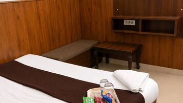 Una habitación de hotel con una cama, una mesita de noche, un televisor montado en la pared y un estante pequeño debajo del televisor.