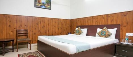 Ein Hotelzimmer mit einer holzgetäfelten Wand, einem Bett mit zwei Kissen, einem Nachttisch mit einer Wasserflasche und einem Sessel.