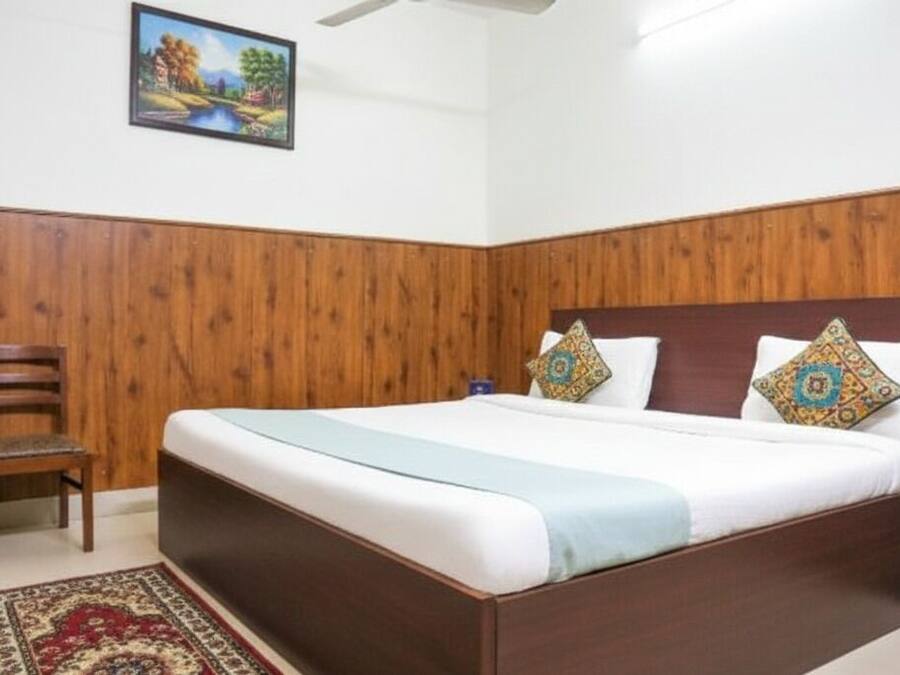 A hotel room with a wooden paneled wall, a bed with two pillows, a nightstand with a water bottle, and a chair.