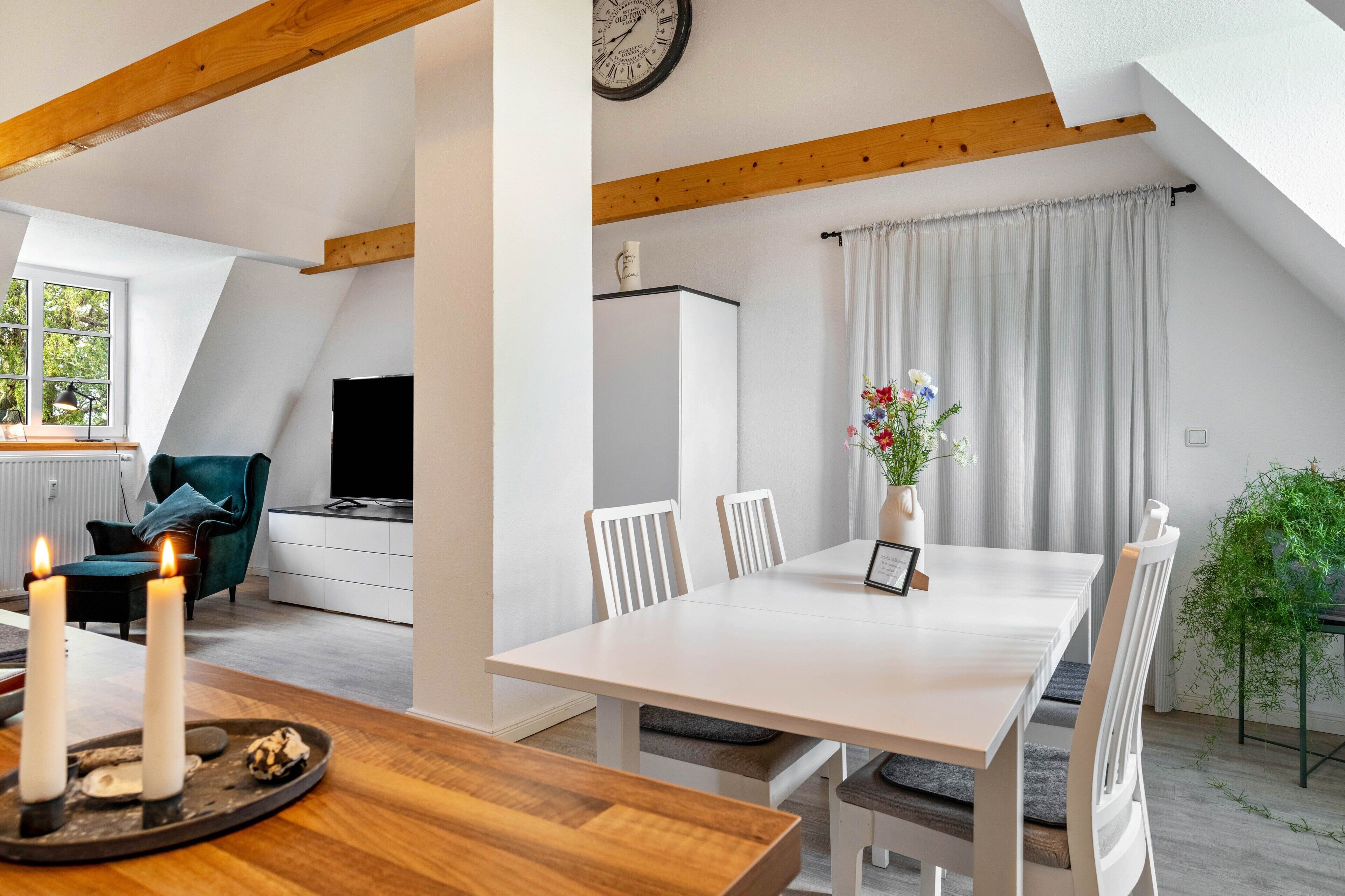 A modern loft-style room with a dining table, white chairs, a clock, and a television.