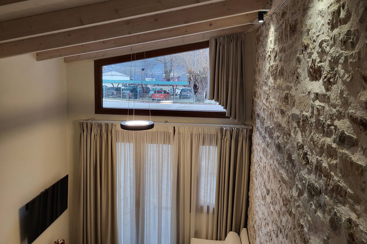 Une pièce dotée d’une grande fenêtre, de poutres en bois au plafond, d’un mur en pierre et d’un luminaire suspendu.