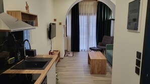 Eine moderne Küche mit Einbauherd, einer Holzarbeitsplatte und einem an der Wand montierten Fernseher. Es gibt eine Sitzecke mit einem grünen Sofa und einem Holztisch.