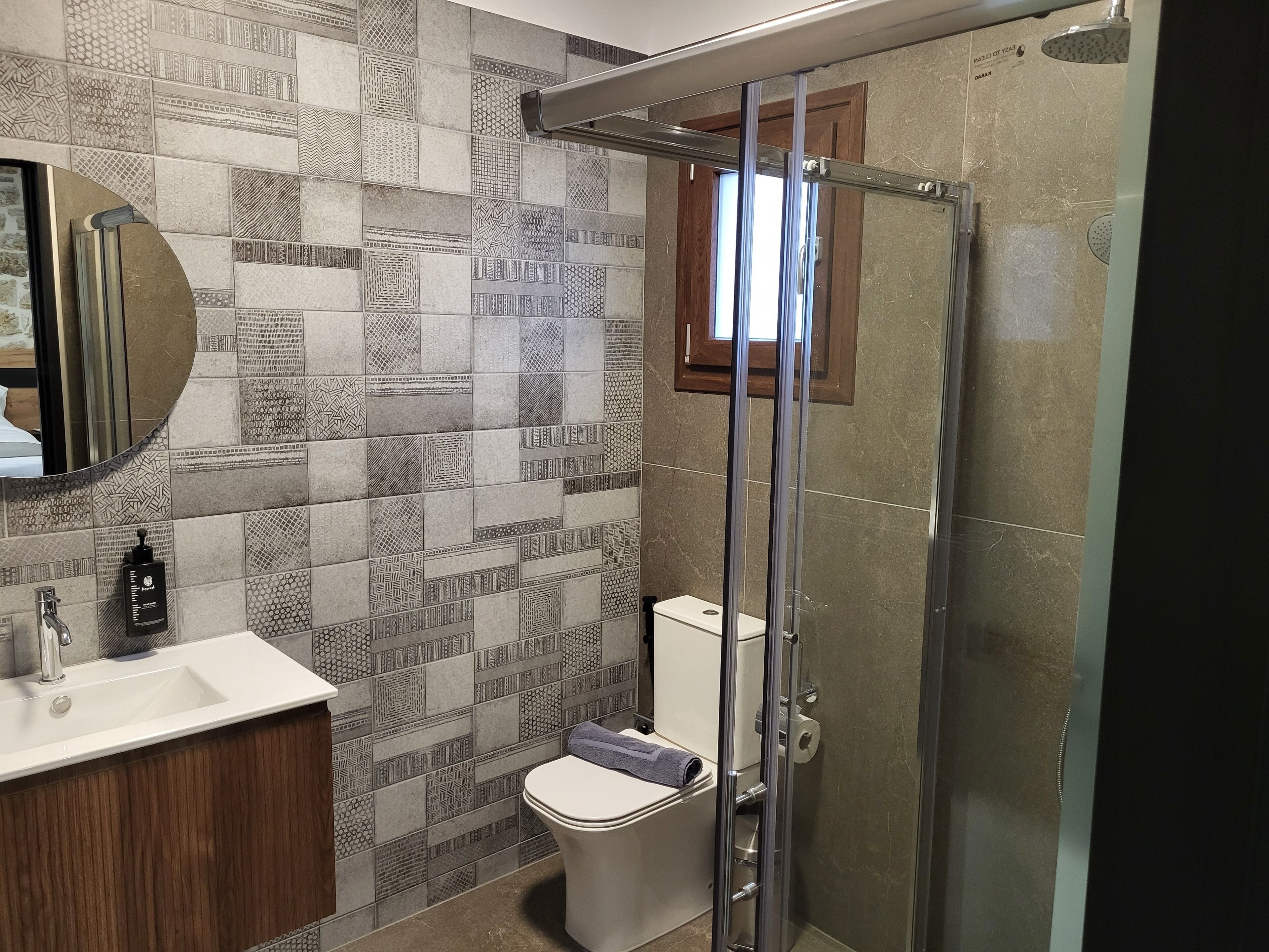 A bathroom with patterned tiles, a glass shower enclosure, a toilet, and a sink with a wooden cabinet.