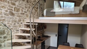 Ein modernes Schlafzimmer im Loft-Stil mit Steinwand, Holzboden und Wendeltreppe, einer Küchenzeile und einem Essbereich.