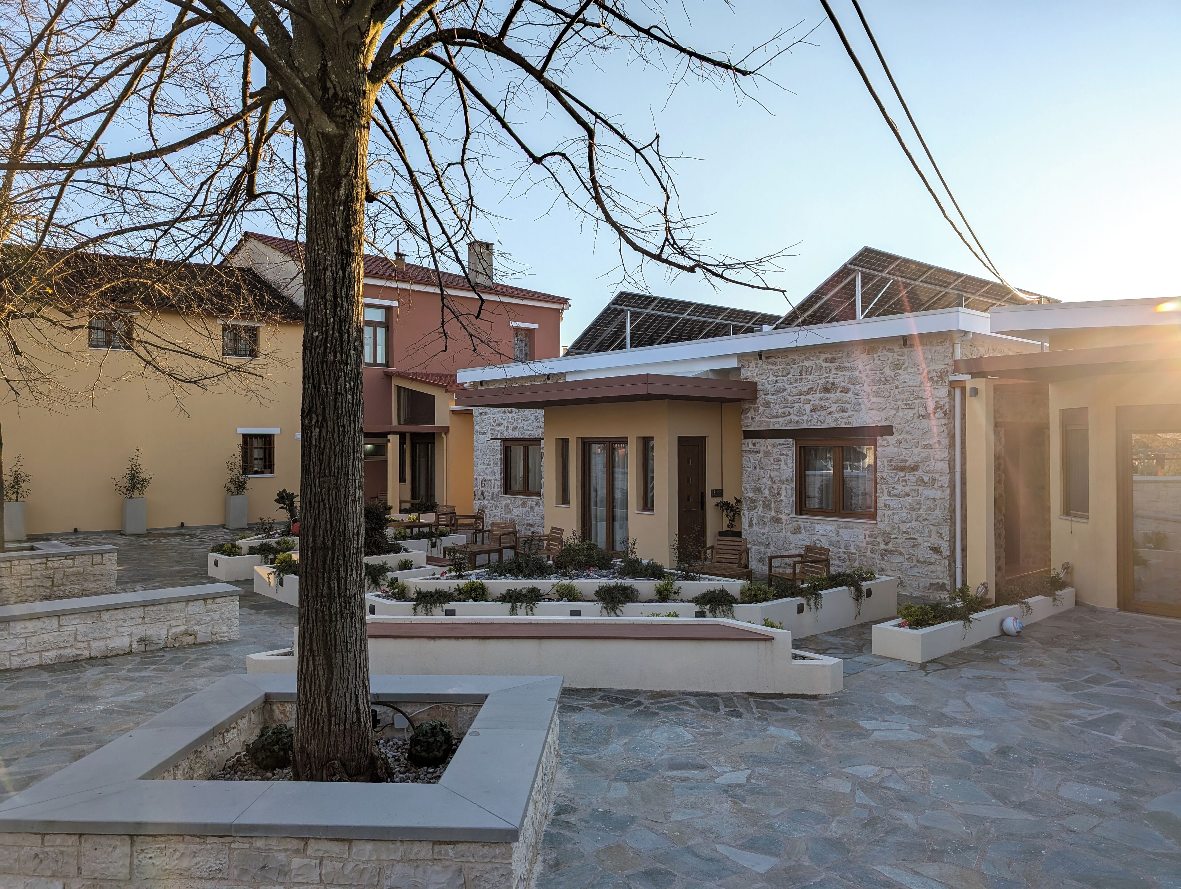 Ein moderner Wohnkomplex mit mehreren Häusern, deren Fassaden aus Stein und Backstein gestaltet sind, einem zentralen Innenhof mit Sitzgelegenheiten sowie Solaranlagen auf den Dächern.