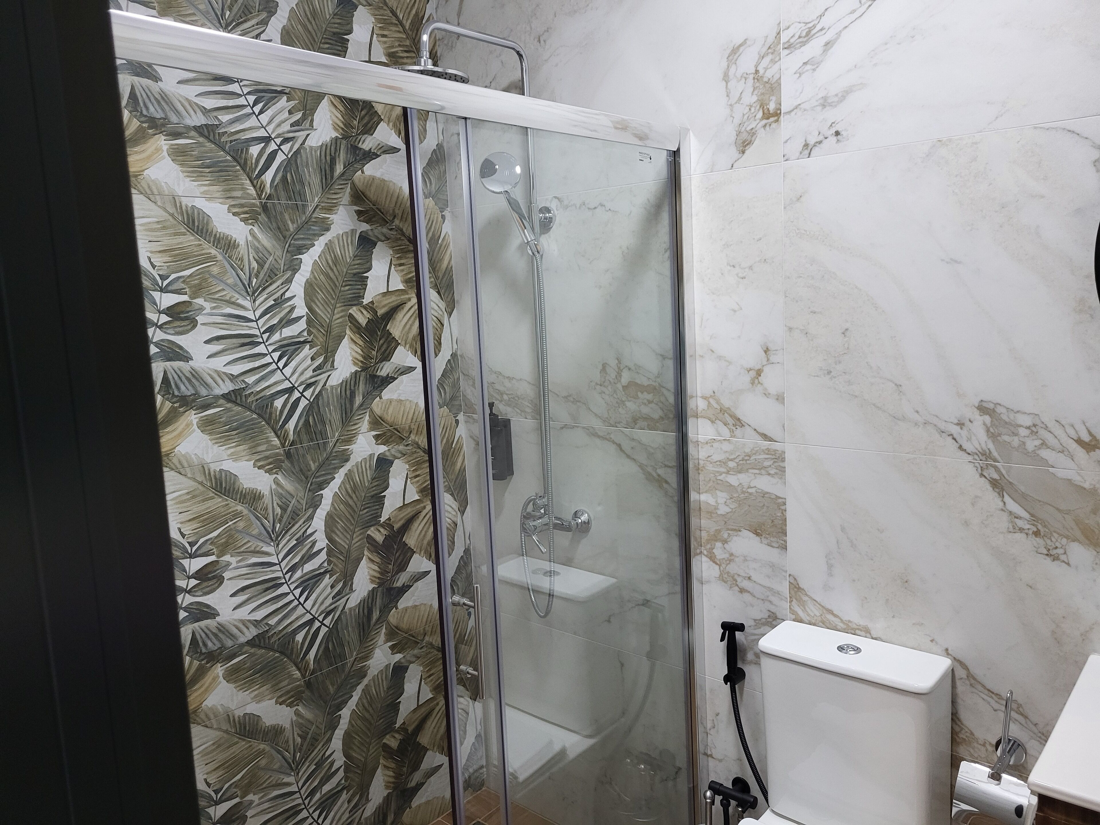 Ducha con puerta de vidrio, inodoro y pared con azulejos de mármol.