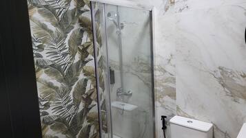 Ducha con puerta de vidrio, inodoro y pared con azulejos de mármol.