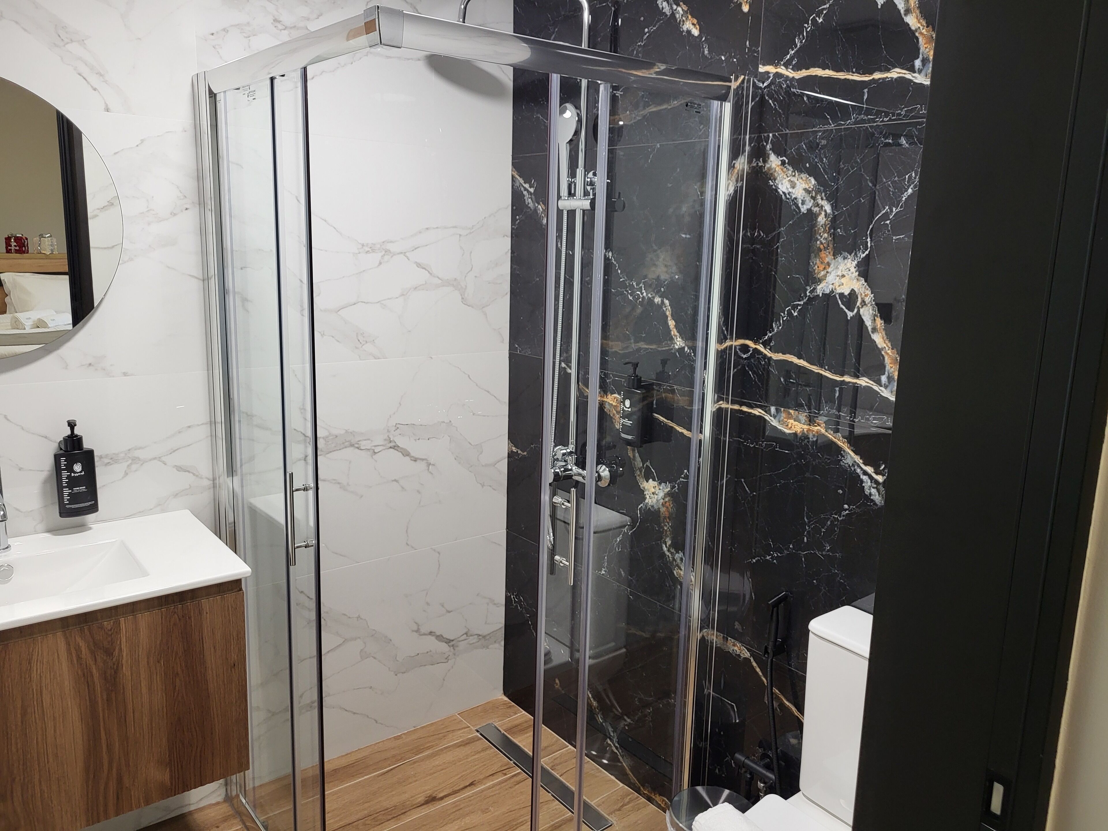 A modern bathroom with a glass-enclosed shower, a wooden vanity, and marble walls.