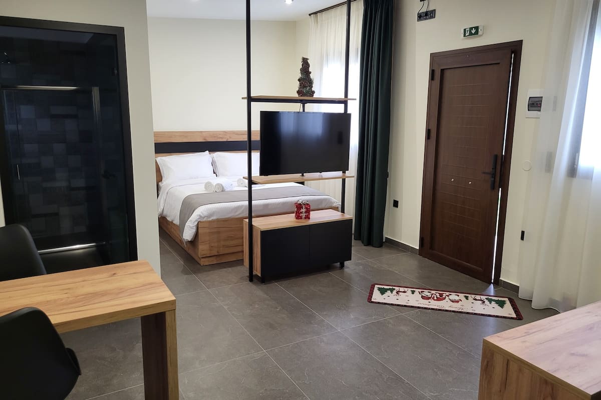 Une chambre d’hôtel avec un lit, une télévision, un bureau en bois, une chaise et une porte.