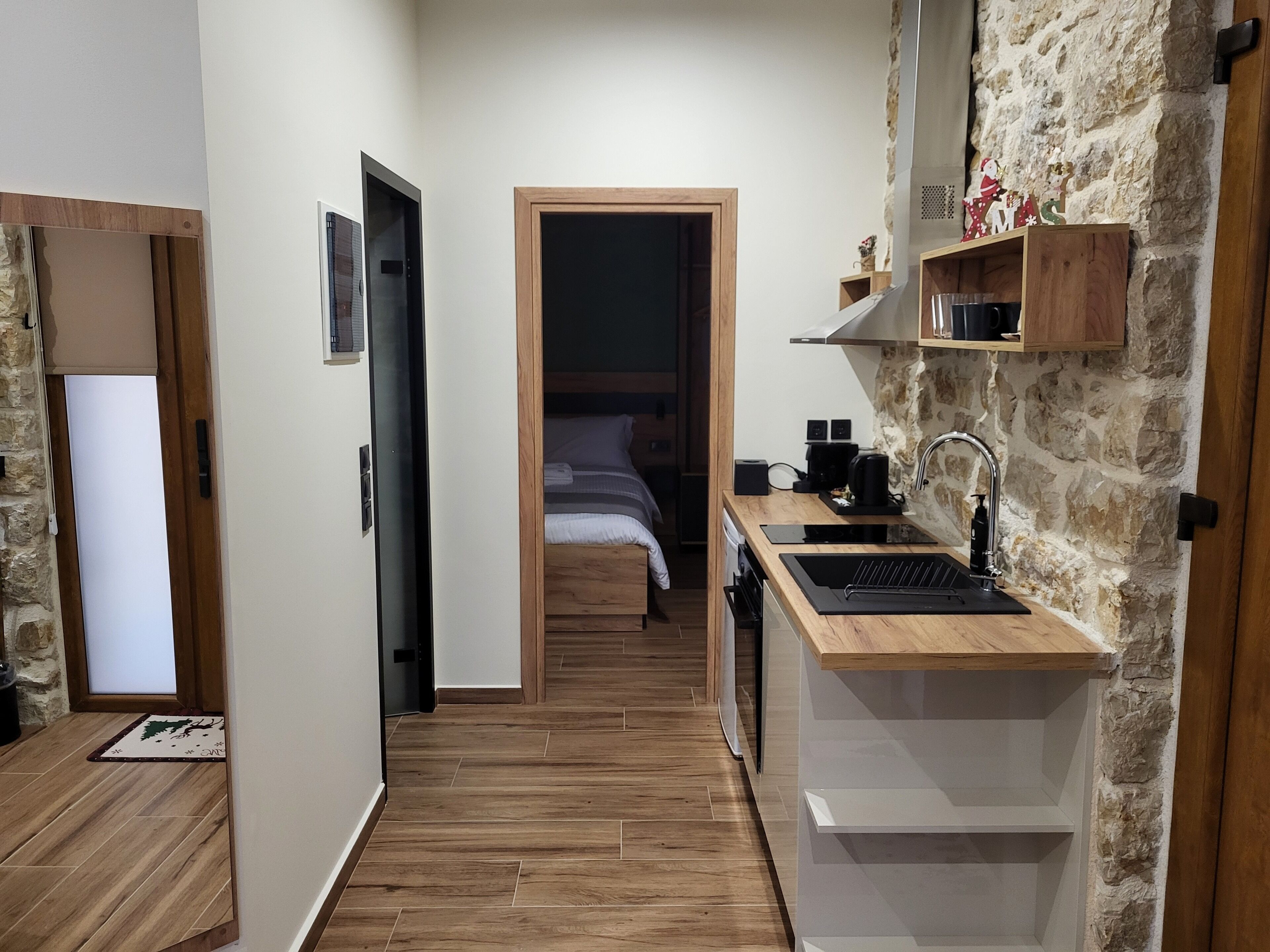 Une cuisine compacte avec un évier, un plan de travail et un mur en pierre. On aperçoit un lit dans la pièce adjacente.