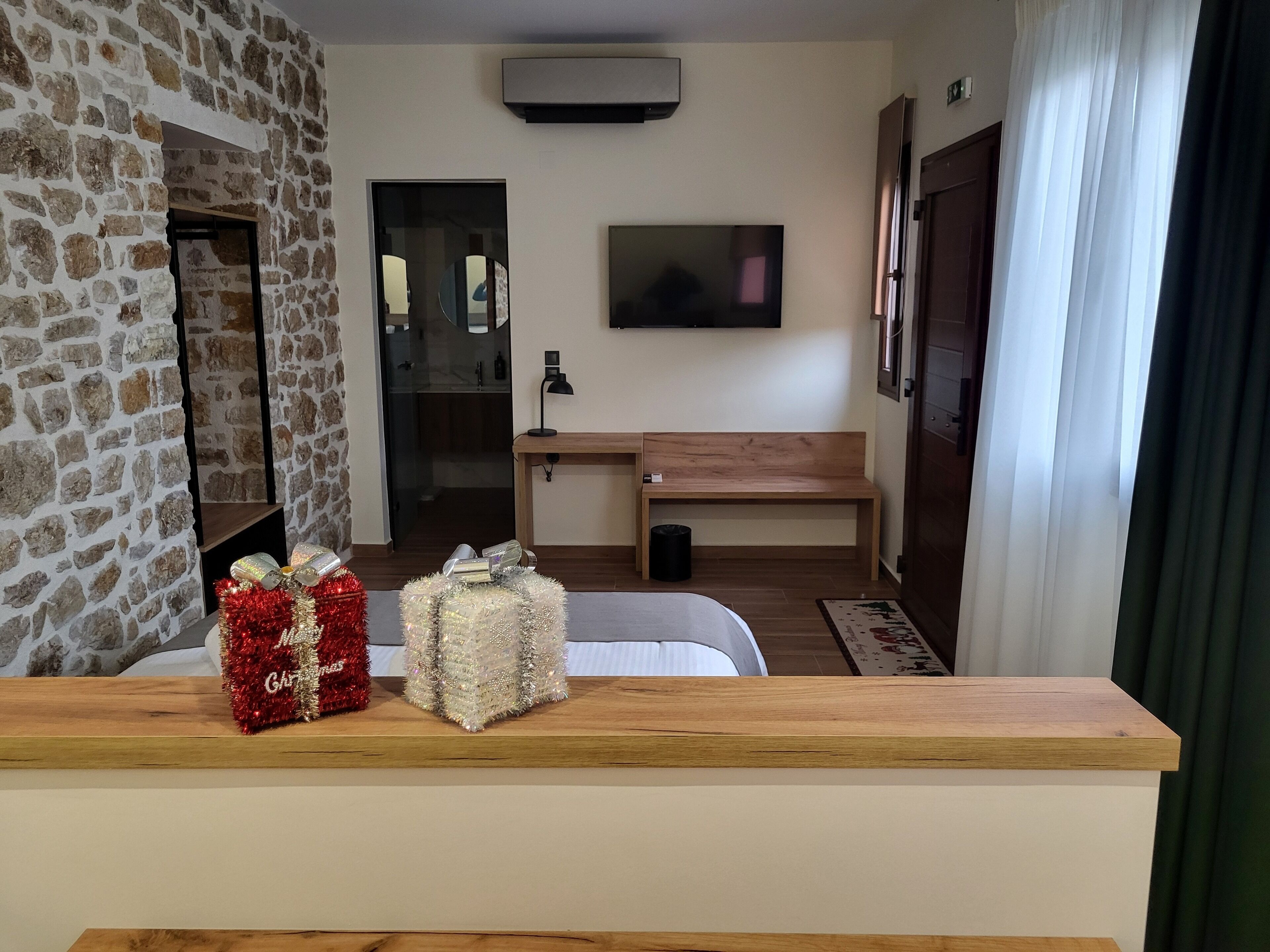 A cozy living room with a stone wall, a wooden bench, a flat-screen TV, and a small table with wrapped gifts.