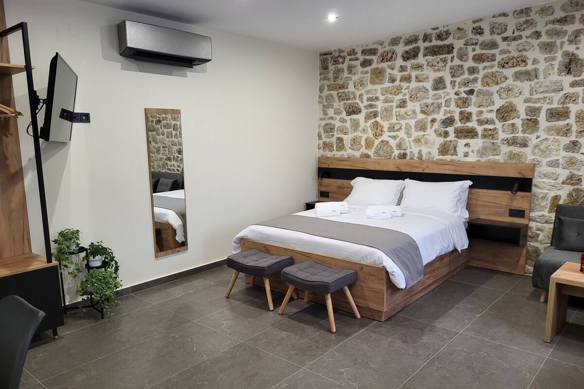 Une chambre à coucher moderne avec un mur en pierre, un cadre de lit en bois, une table de chevet et un petit tabouret.