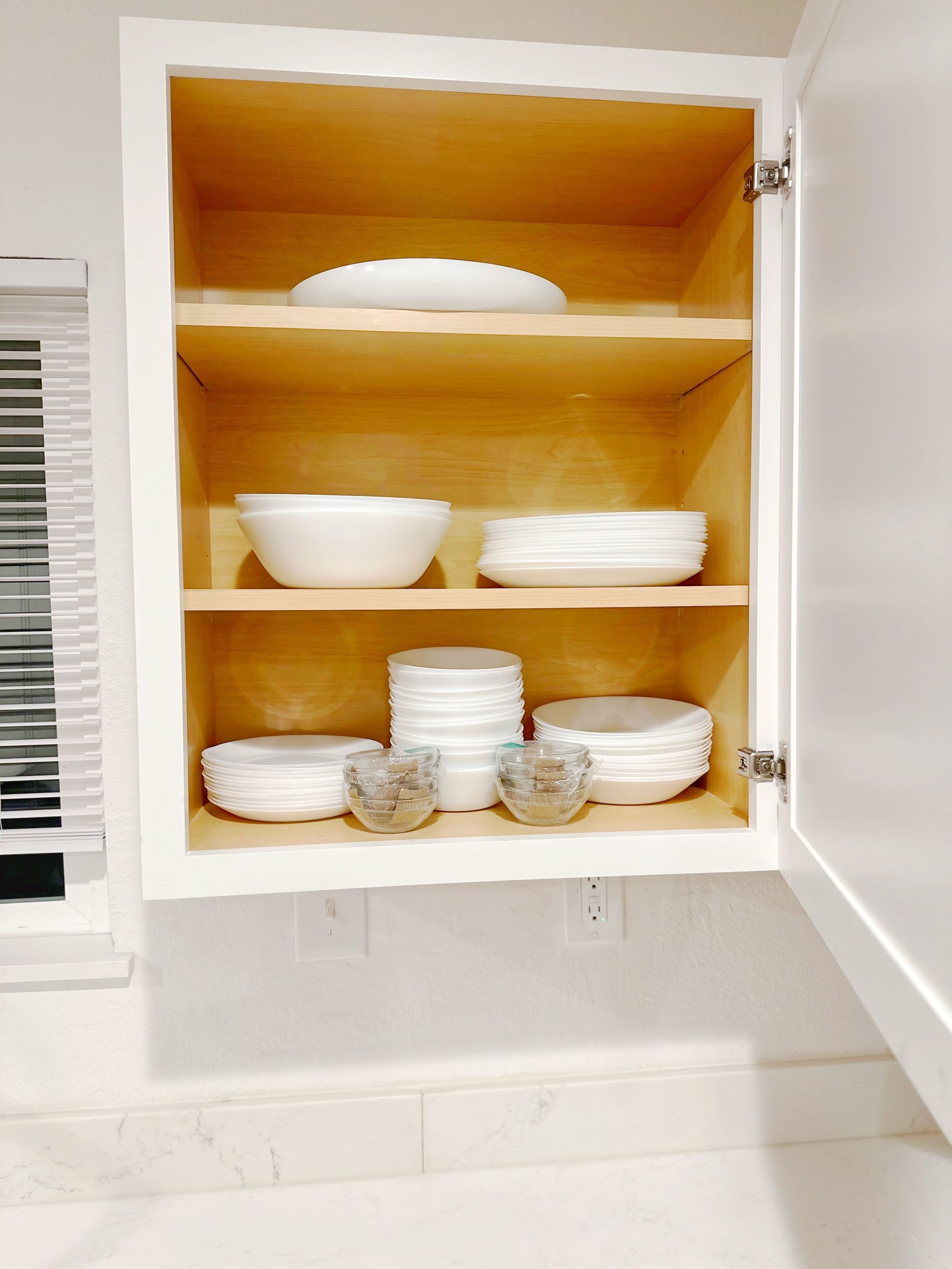 Ein weißes Schrank mit drei Einlegeböden, auf denen weiße Schalen und Teller stehen.