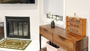 Una sala de estar con chimenea, un televisor montado en una pared de ladrillo, un escritorio de madera con un letrero de bienvenida y decoración en la pared.