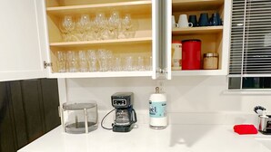 Una cocina compacta con armarios blancos, cafetera, dispensador de agua y lavavajillas.