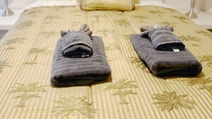Una cama bien hecha con una colcha a rayas, dos toallas dobladas, un cojín decorativo y una obra de arte en la pared sobre la cama.