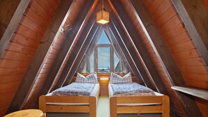 A room with two wooden beds, a hanging light fixture, and a window at the end of the room.