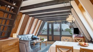 A loft-style room with a sloped ceiling, a sofa, a dining table, and a television.