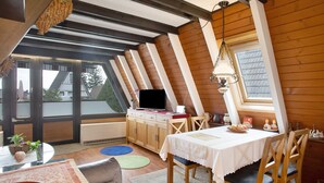 A cozy attic room with a dining table, chairs, a TV, and a window with a view.