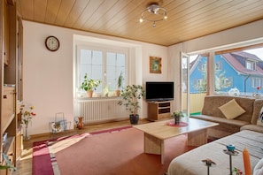 Een woonkamer met een televisie, bank, salontafel en potplanten.