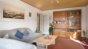 Ein Wohnzimmer mit einer Couch, einem Holztisch, einem Bücherregal und einem gerahmten Landschaftsbild.