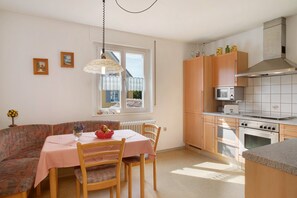 Een keuken met een eettafel, stoelen, een radiator, een magnetron, een oven en houten kastjes.